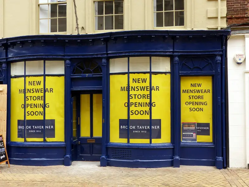 A navy-painted shop front with yellow hoardings on a pedestrianised street in Stamford